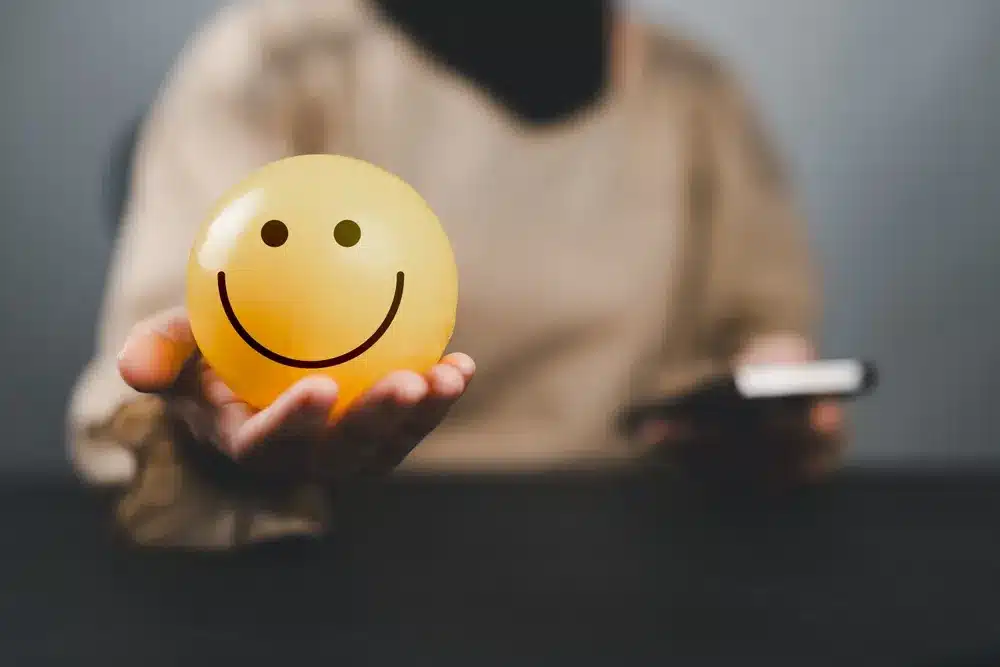 Person holding a smiley face with a phone in their hand