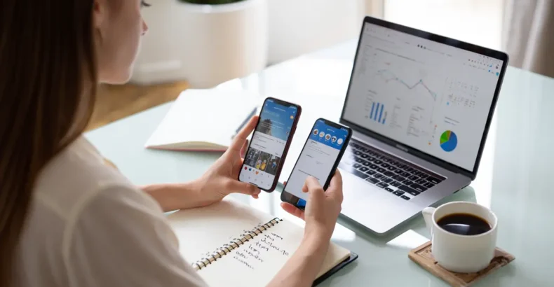 Person holding two mobile phones in front of a laptop
