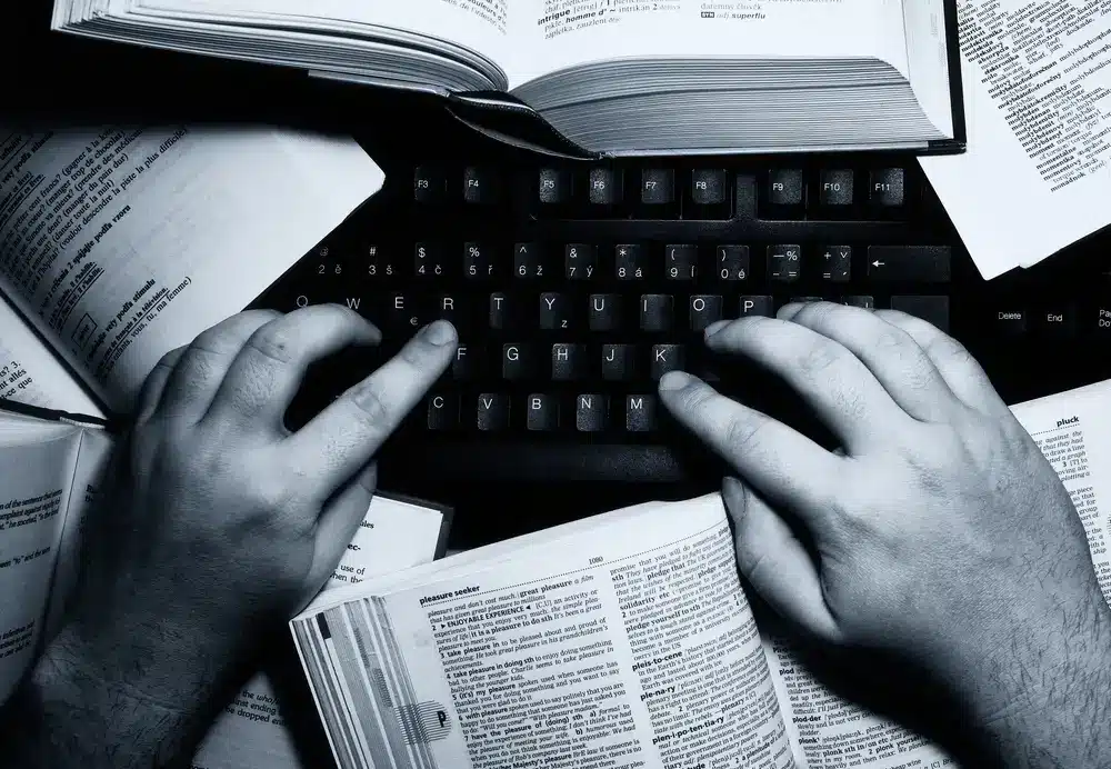 Person's hands typing on a keyboard surrounded by text books